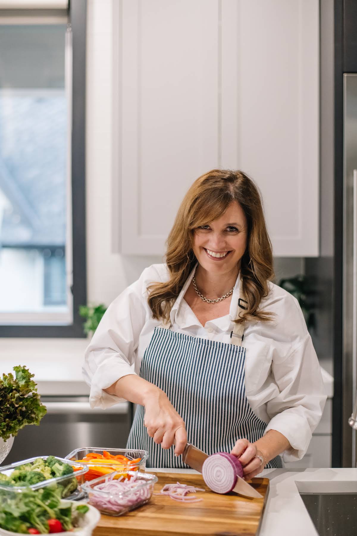 Holly Nilsson smiling while slicing a red onion in her kitchen